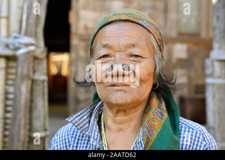 Ziro valle, Arunachal Pradesh, India - 08 gennaio 2019: vecchia donna Apatani davanti alla porta di casa con la faccia di tribali tattoo e legno nero tappi naso, Foto Stock