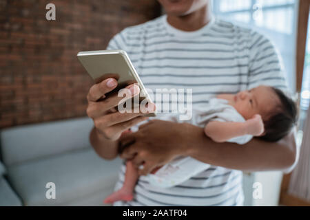 Padre che porta la figlia quando si utilizza il telefono cellulare Foto Stock