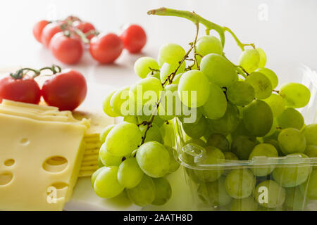 Uva verde, il formaggio e i pomodori vicino sul marmo chiaro dello sfondo. Foto Stock