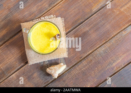 Golden Curcuma latte in un bicchiere di vetro con la cannella e lo zenzero su un tavolo di legno. Foto Stock