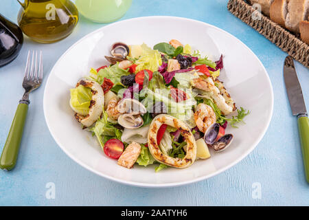 L'insalata di frutti di mare. Deliziosa insalata fresca di gamberi, calamari, gamberetti, cozze e mescolate le foglie di lattuga, rucola nel piatto bianco sulla vecchia scheda di legno Foto Stock