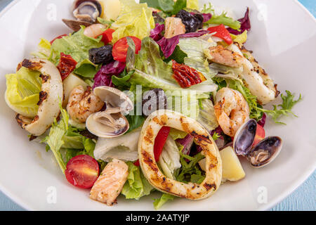 L'insalata di frutti di mare. Deliziosa insalata fresca di gamberi, calamari, gamberetti, cozze e mescolate le foglie di lattuga, rucola nel piatto bianco sulla vecchia scheda di legno Foto Stock