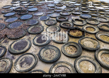 Mare coperta con la vecchia gomma di pneumatici vettura parzialmente assorbita nella sabbia bagnata, sfondo astratto Foto Stock