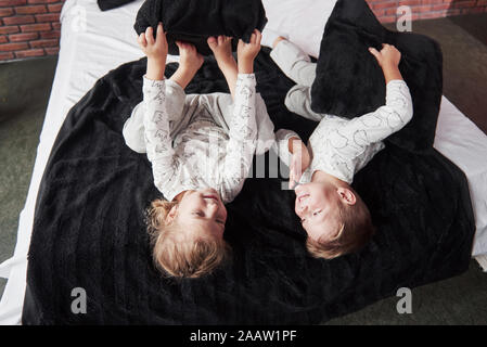 Bambini cattivi piccolo ragazzo e ragazza in scena una lotta di cuscini sul letto in camera da letto. A loro piace quel tipo di gioco Foto Stock