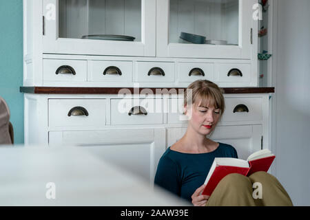 Ritratto di donna seduta in cucina per leggere un romanzo Foto Stock