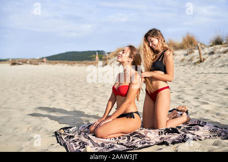 Giovane donna braidng i capelli del suo amico sulla spiaggia Foto Stock