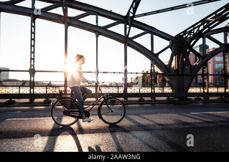 Giovane ciclista su un ponte al tramonto Foto Stock