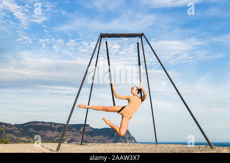 Donna pratica fly dance gravità lo yoga pone in una amaca all'aperto con vista montagna. Uno stile di vita sano, attivo della donna. Foto Stock