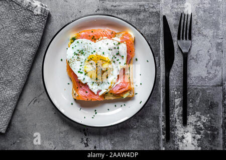 Direttamente sopra il colpo di pane tostato con salmone e a forma di cuore ad uovo fritto nella piastra sulla tavola Foto Stock