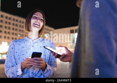 Coppia felice nella città di notte di controllo sui loro telefoni, Berlino, Germania Foto Stock