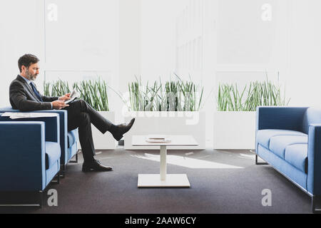 Imprenditore maturo seduto in area di attesa rivista di lettura Foto Stock