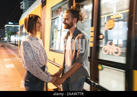 Coppia sorridente tenendo le mani e guardando a vicenda con un tram in background, Berlino, Germania Foto Stock