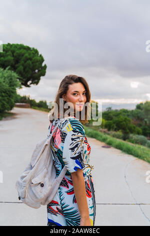 Ritratto di sorridente giovane donna con zaino passeggiando nel parco Foto Stock