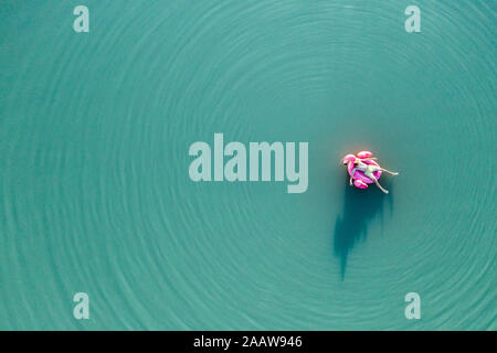 Giovane con flamingo piscina galleggiante sul lago Foto Stock