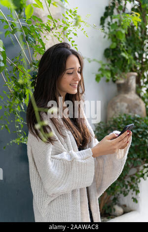 Giovane donna indossa cardigan e utilizza lo smartphone Foto Stock