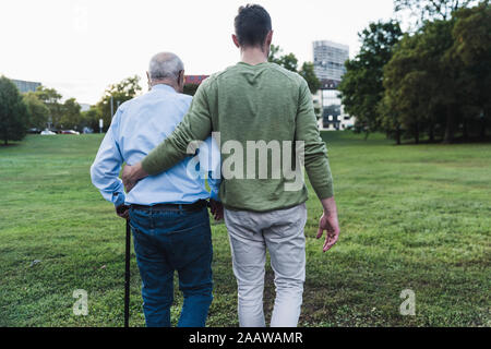 Vista posteriore del giovane uomo che assiste il suo nonno a piedi Foto Stock