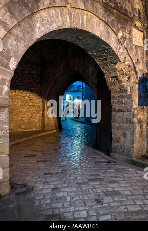 Ingresso ad arco con muri in pietra e la vecchia città di Ioannina di notte, Grecia Foto Stock