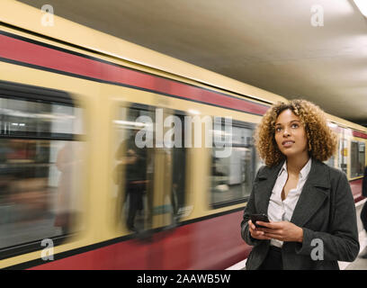 Donna con telefono cellulare nella stazione della metropolitana come il treno arriva in Foto Stock