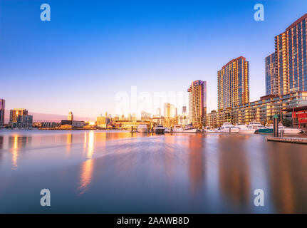 Edifici illuminati da fiume a Melbourne Docklands contro il cielo blu al tramonto, Victoria, Australia Foto Stock