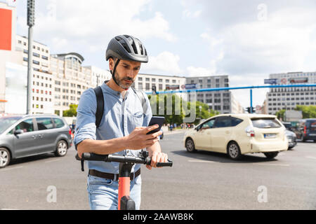 Imprenditore guardando lo smartphone il pendolarismo su scooter elettrico nella città di Berlino, Germania Foto Stock