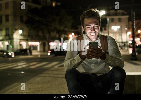 Ritratto di felice giovane tramite telefono cellulare nella città di notte, Lisbona, Portogallo Foto Stock