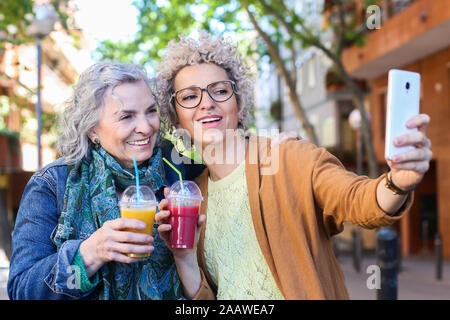 Senior madre con sua figlia adulta prendendo selfie nella città Foto Stock