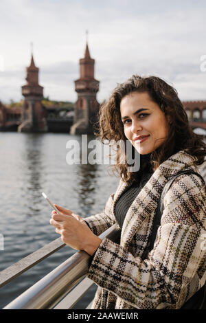 Ritratto di una donna con lo smartphone in città al ponte Oberbaum, Berlino, Germania Foto Stock