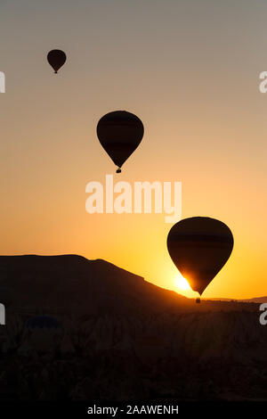 Silhouette mongolfiere che sorvolano il paesaggio durante il tramonto a Goreme, Cappadocia, Turchia Foto Stock