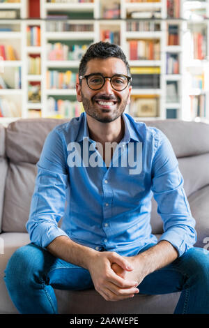Ritratto di felice giovane uomo seduto sul divano di casa Foto Stock