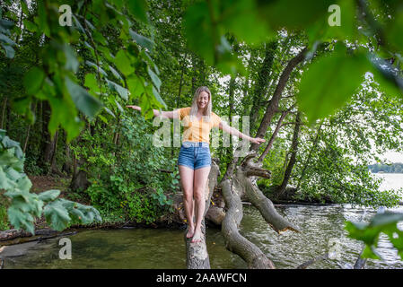 Donna sorridente in equilibrio su un tronco di albero sul lungolago Foto Stock