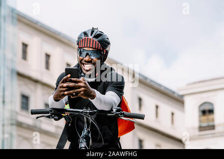 Felice elegante giovane con bicicletta, smartphone e messenger bag in città Foto Stock