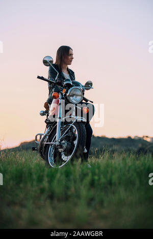 Giovane donna con moto vintage in scena rurale di godersi il tramonto Foto Stock