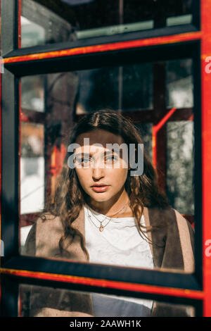 Giovane donna in una cabina telefonica, guardando la fotocamera Foto Stock