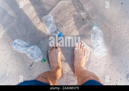 L'uomo con i piedi sul mare circondato da le bottiglie di plastica vuote, vista dall'alto Foto Stock
