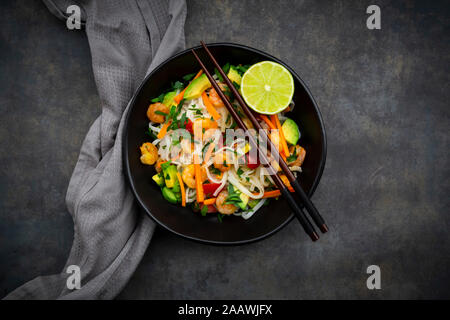 Angolo di alta vista di cellophane tagliatelle con gamberi e verdure servita nella ciotola sul tavolo Foto Stock