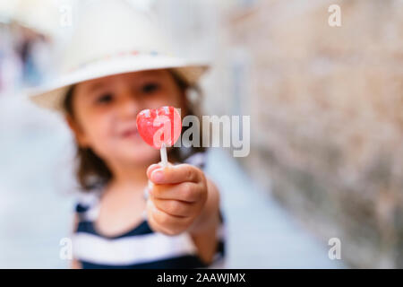 Poco la mano della bambina tenendo a forma di cuore lecca-lecca, close-up Foto Stock