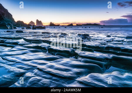 Nuova Zelanda, Sud isola rocciosa costa del mare al tramonto con Motukiekie spiaggia mare pile in distanza Foto Stock