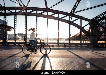 Giovane ciclista su un ponte al tramonto Foto Stock