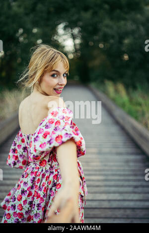 Ritratto di felice giovane donna che indossa abiti estivi con disegno floreale sul Boardwalk tenendo la mano Foto Stock