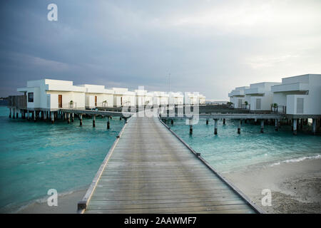 Una diminuzione del punto di vista del molo che conduce verso ville oltre il mare di Maldive Foto Stock