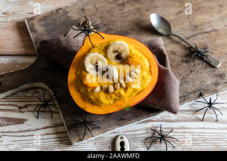 Angolo di alta vista di zucca con faccia antropomorfa e decorazioni su un tavolo di legno durante il periodo di Halloween Foto Stock