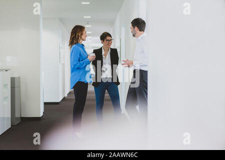Imprenditore e due imprenditrici avente una pausa caffè parlando sul corridoio di office Foto Stock