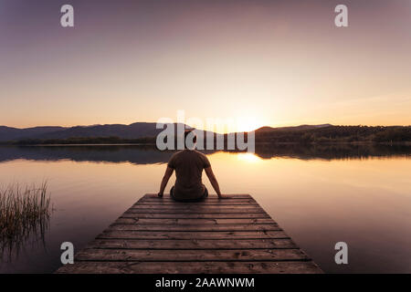 Silhouette di un uomo seduto su una passerella di legno al tramonto Foto Stock