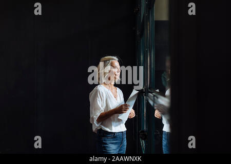 Casual imprenditrice matura guardando fuori della finestra in ufficio loft Foto Stock