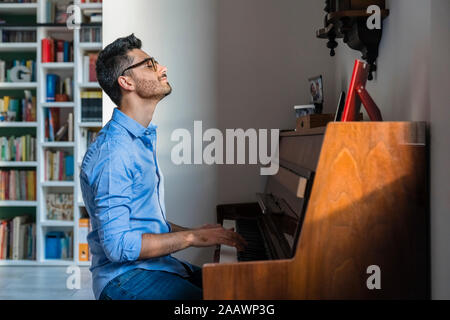 Sorridente giovane con gli occhi chiusi suonare il pianoforte a casa Foto Stock
