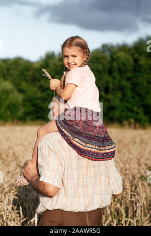 Ritratto di felice bambina su nonno spalle in un campo di avena Foto Stock