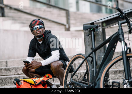 Elegante giovane con bicicletta, smartphone e messenger bag in città Foto Stock