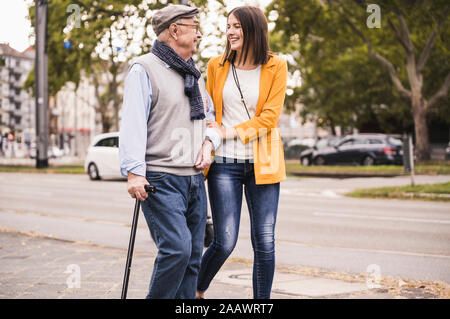 Nipote di adulto assistere suo nonno passeggiando con bastone Foto Stock