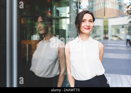Ritratto di fiducioso giovane imprenditrice riflessa nella parte anteriore in vetro, Berlino, Germania Foto Stock