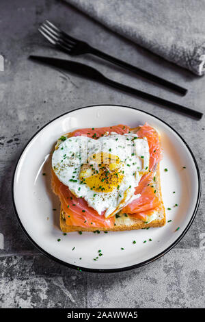 Close-up di pane tostato con salmone e a forma di cuore ad uovo fritto nella piastra sulla tavola Foto Stock